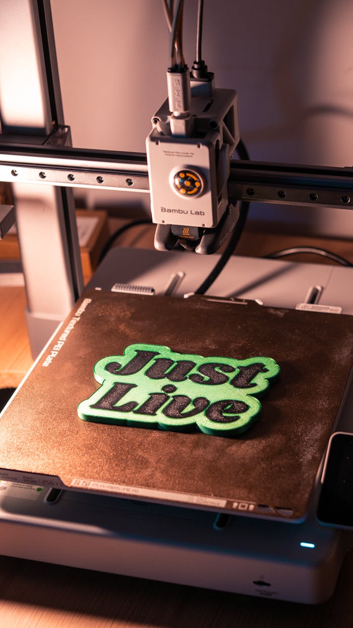 our-experience A 3D printer crafting 'Just Live' text in a workshop setting. Ideal for digital technology and innovation themes.